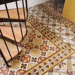 Escalier en bois et rampe métallique sur carreaux de ciment à motifs jaunes, rouges et gris