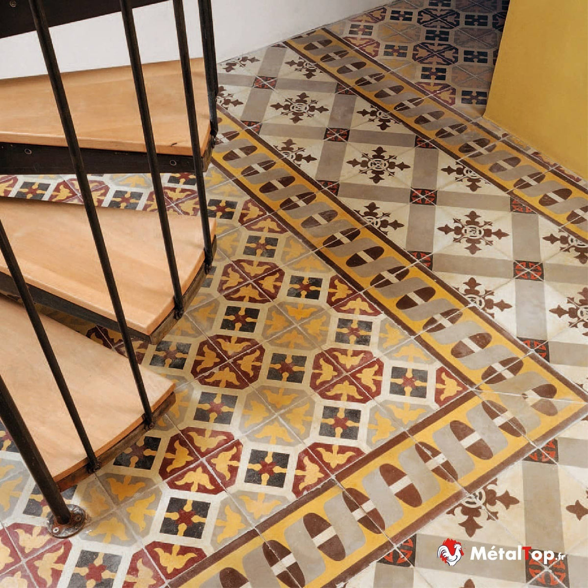 Escalier en bois et rampe métallique sur carreaux de ciment à motifs jaunes, rouges et gris