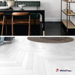 Sol en parquet blanc à chevrons, tapis rond, table noire et chaises en bois