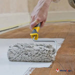 Rouleau à poils gris appliquant un enduit sur une zone blanche protégeant un parquet en bois