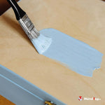 Application de peinture bleu pastel au pinceau sur un panneau de bois clair