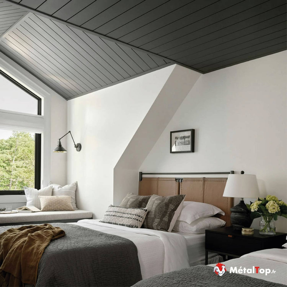 Chambre mansardée aux lambris gris, lits gris, tête de lit en cuir et banquette sous la fenêtre