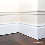Plinthe et moulure blanches dans un angle de pièce, posées sur un parquet en bois brun