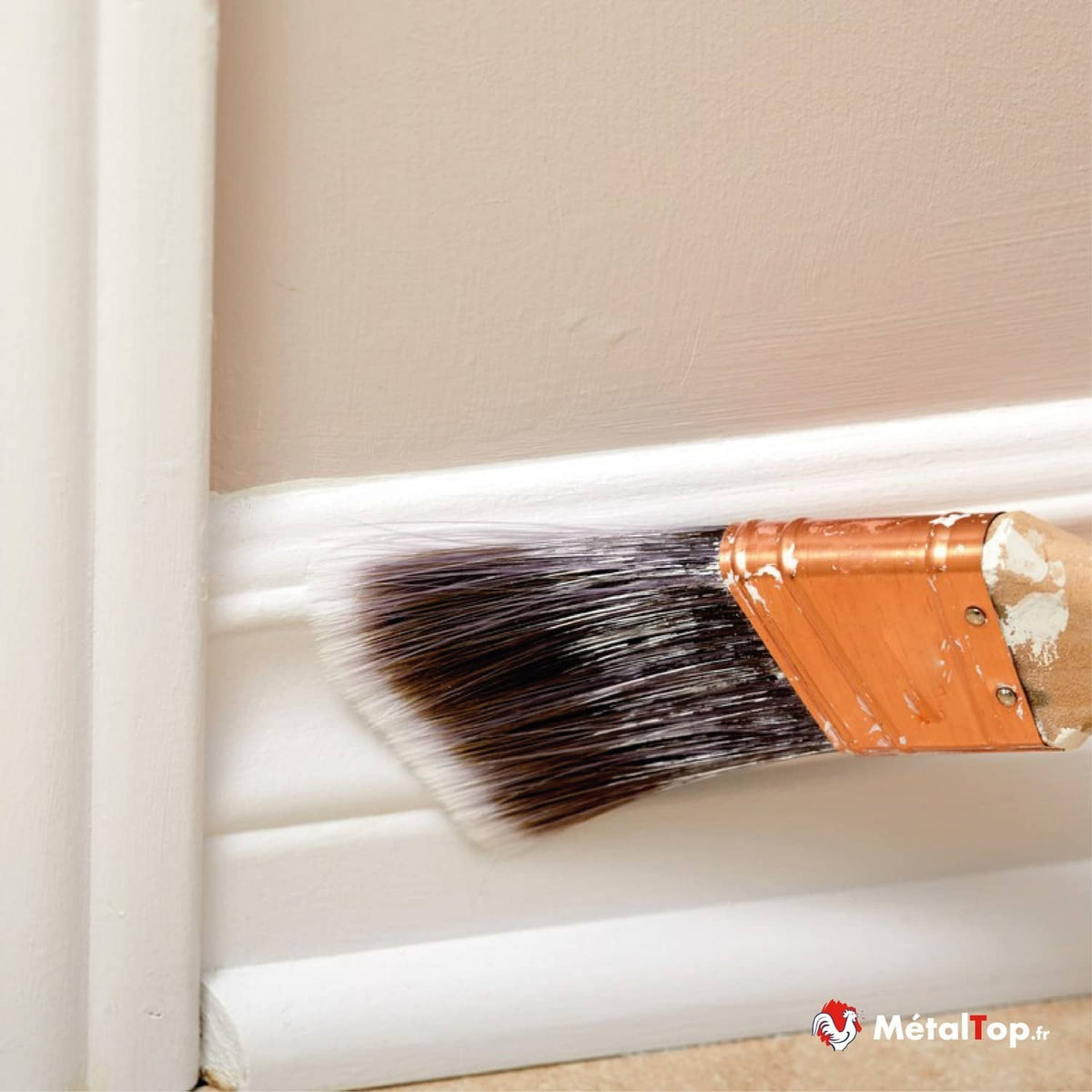 Pinceau appliquant de la peinture blanche sur une plinthe au pied d'un mur beige