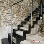 Escalier métallique noir à marches suspendues, garde-corps à câbles, mur en pierre apparente