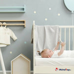 Bébé allongé dans un lit blanc à barreaux, chambre aux murs gris et décorations bleu pastel