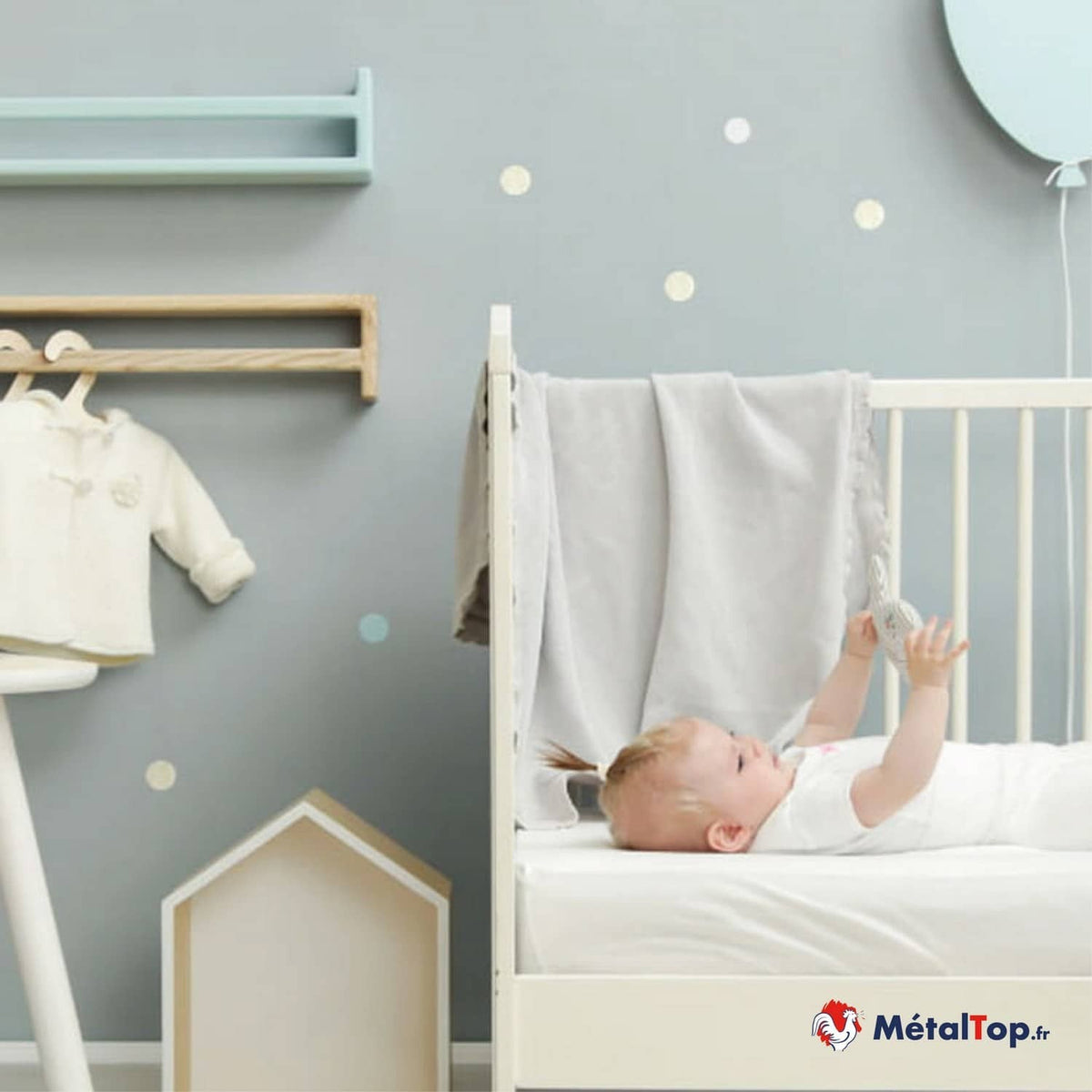 Bébé allongé dans un lit blanc à barreaux, chambre aux murs gris et décorations bleu pastel