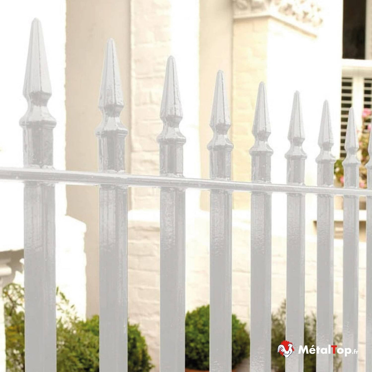 Clôture métallique blanche à pointes ornementales devant une façade en briques peintes