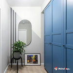 Couloir avec armoire bleue, miroir ovale, plante verte sur tabouret noir et tableau au sol