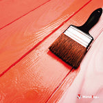Pinceau appliquant une peinture rouge orangé sur des planches en bois