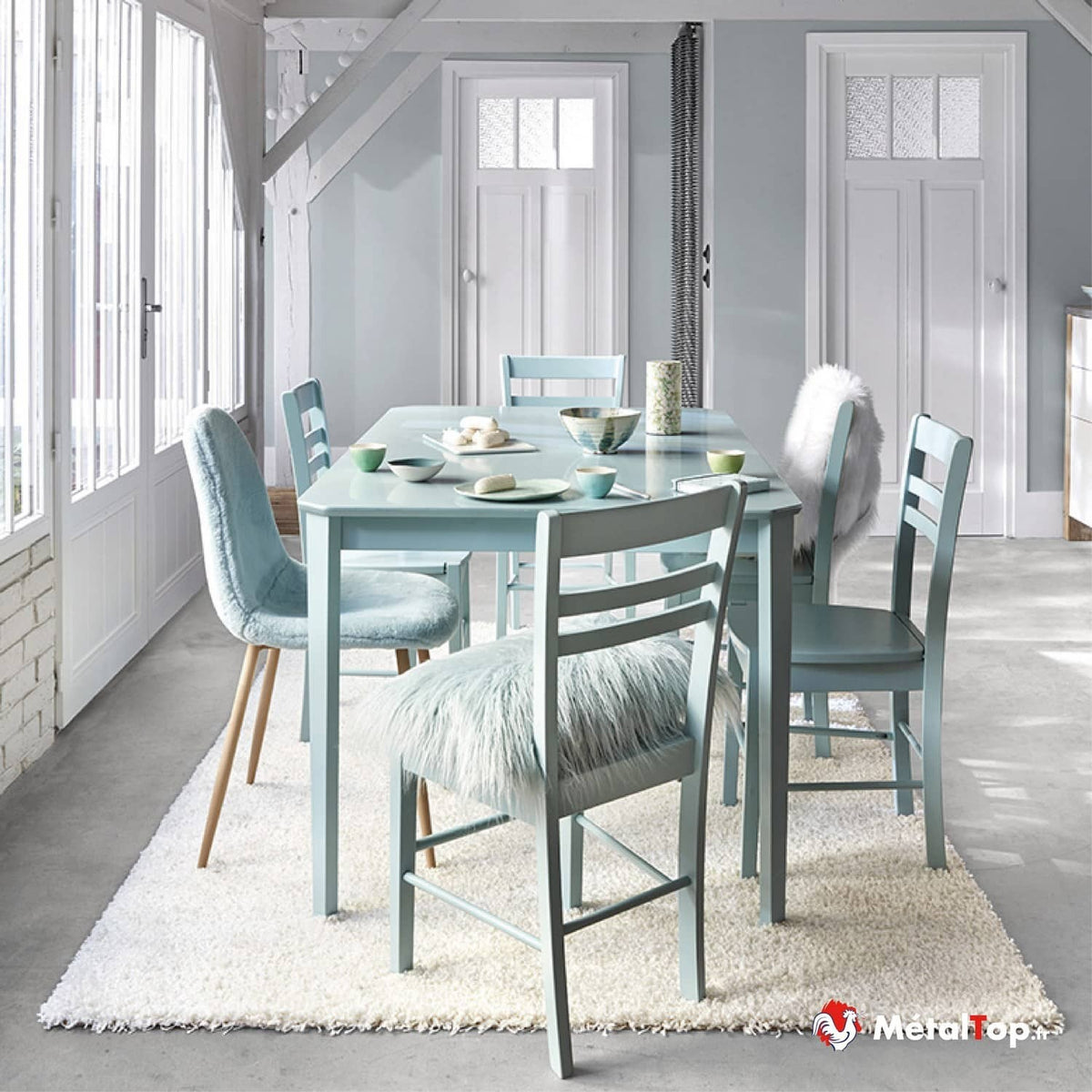 Salle à manger lumineuse avec table et chaises bleu pastel, coussins en fourrure et tapis blanc