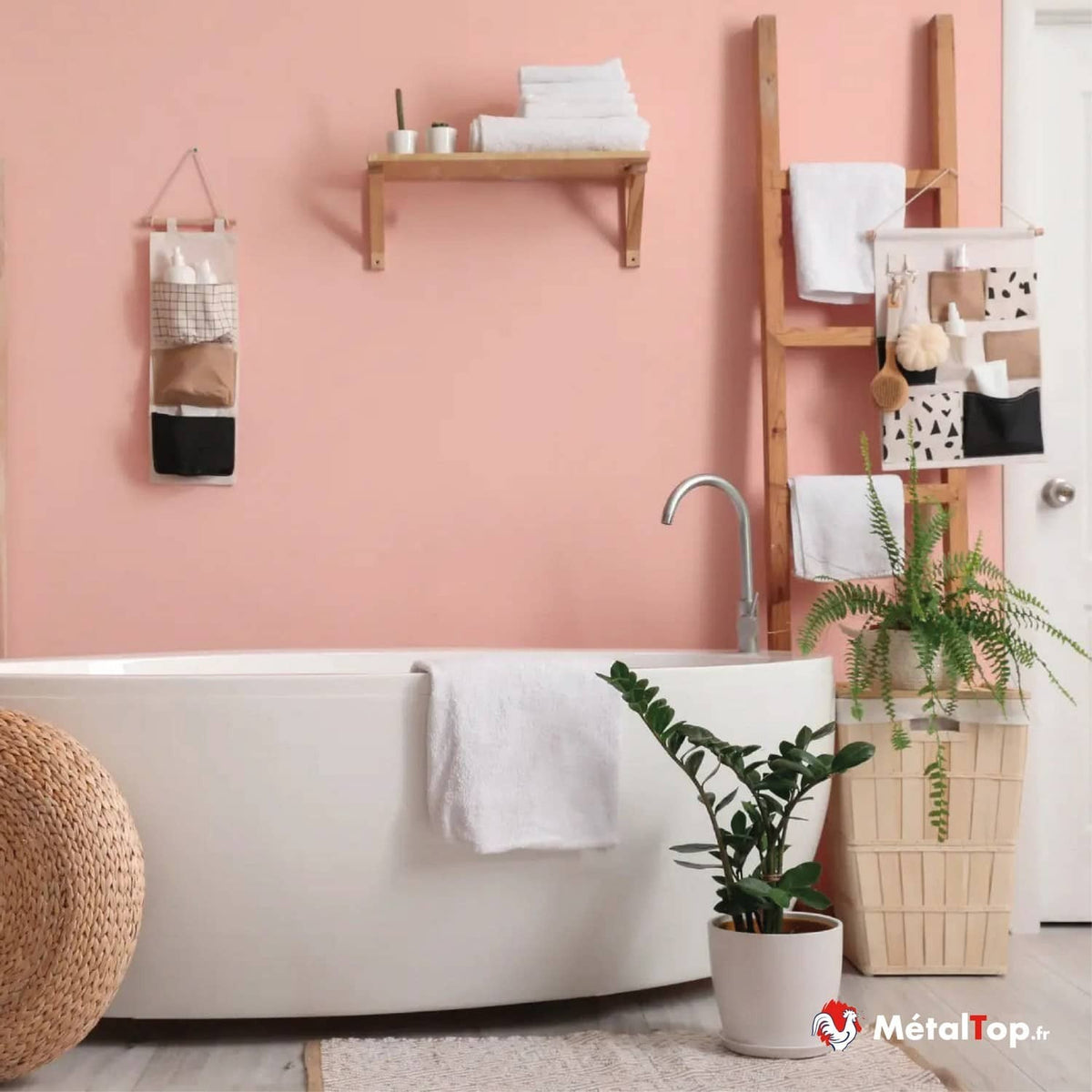 Salle de bain aux murs roses avec baignoire blanche, serviettes, échelle en bois et plantes vertes
