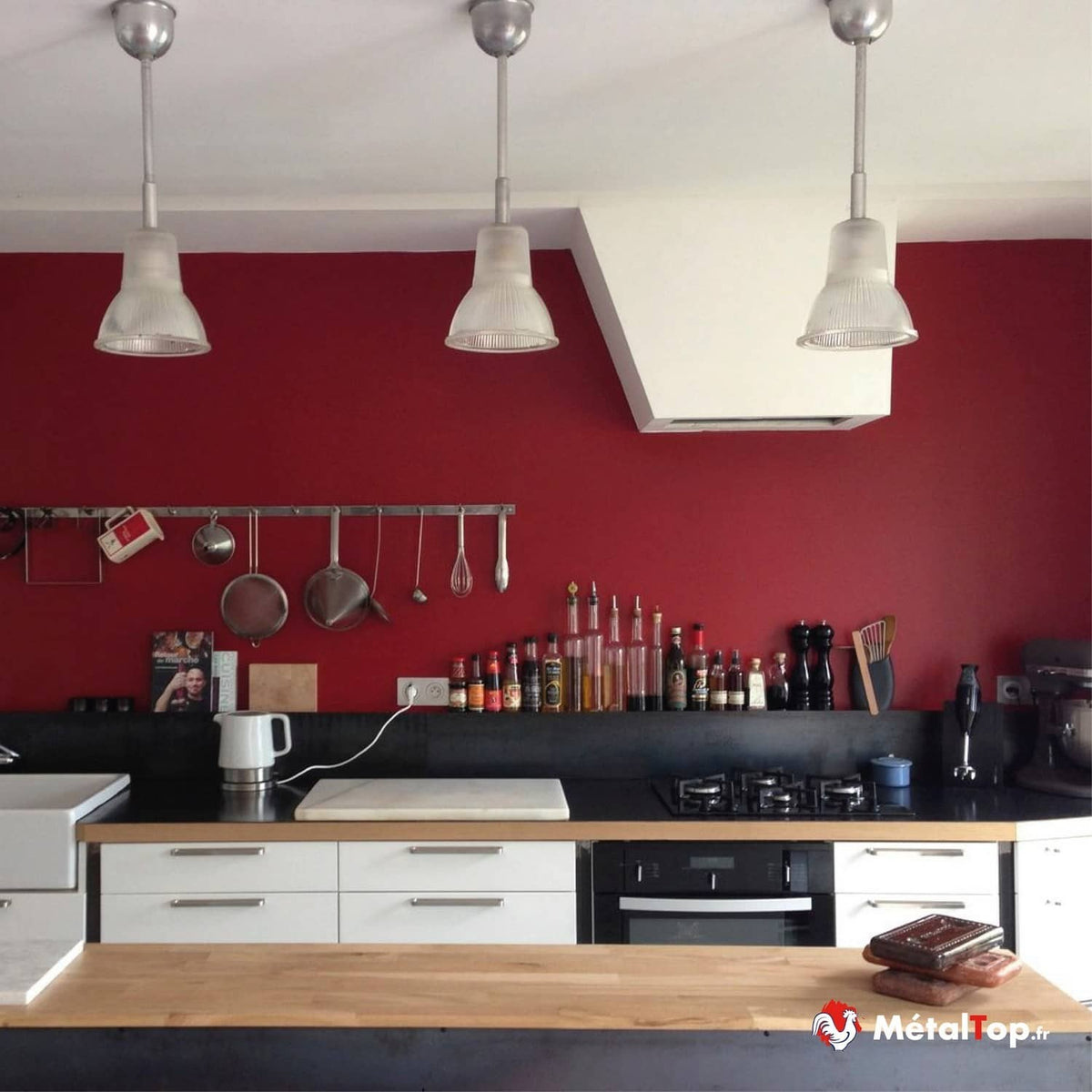 Cuisine au mur rouge, plan de travail en bois et noir, suspensions, ustensiles et flacons d'épices