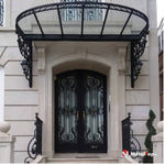 Auvent en verre et fer forgé noir au-dessus d'une double porte d'entrée ornée de ferronnerie