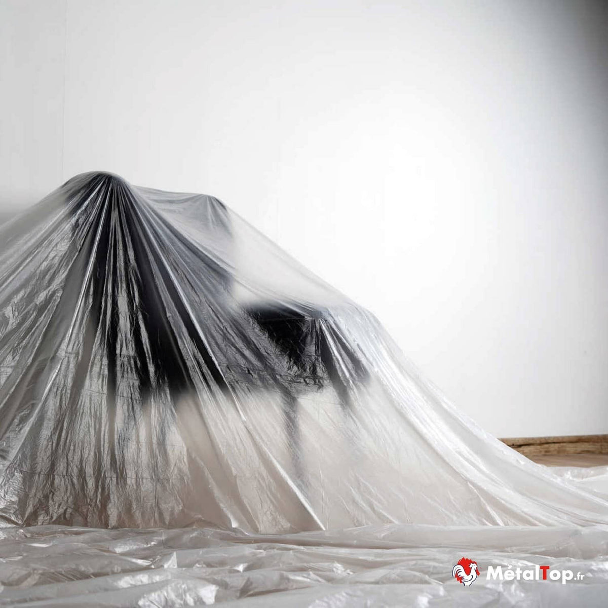 Objet recouvert d'une bâche plastique transparente, posée sur un sol protégé par du film plastique