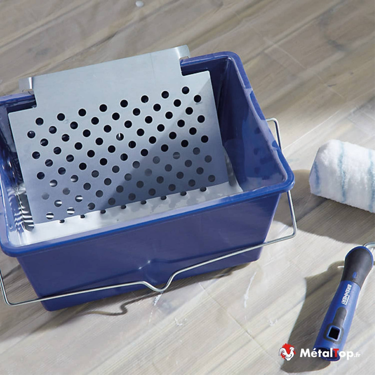 Bac à peinture bleu avec grille perforée, rouleau et manche posés sur un parquet clair