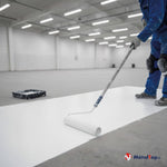 Ouvrier en combinaison bleue appliquant une peinture blanche au rouleau sur un sol d'entrepôt
