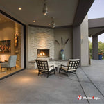 Terrasse couverte en béton avec cheminée en pierre, deux fauteuils noirs à coussins crème