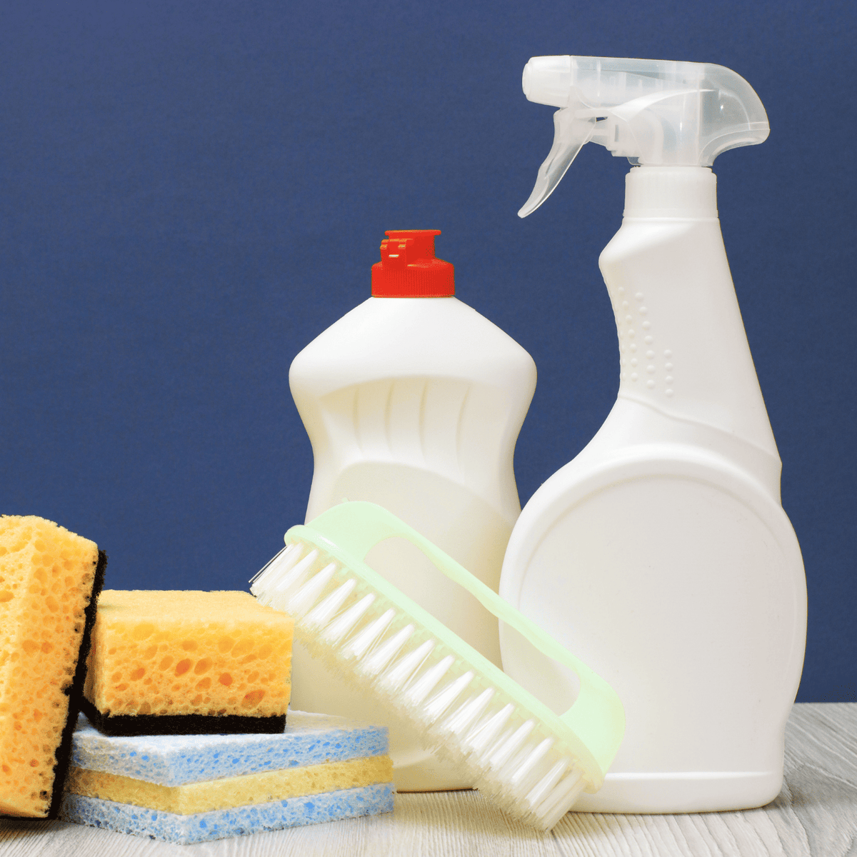 Produits de nettoyage : flacon de liquide vaisselle, spray blanc, brosse verte et éponges