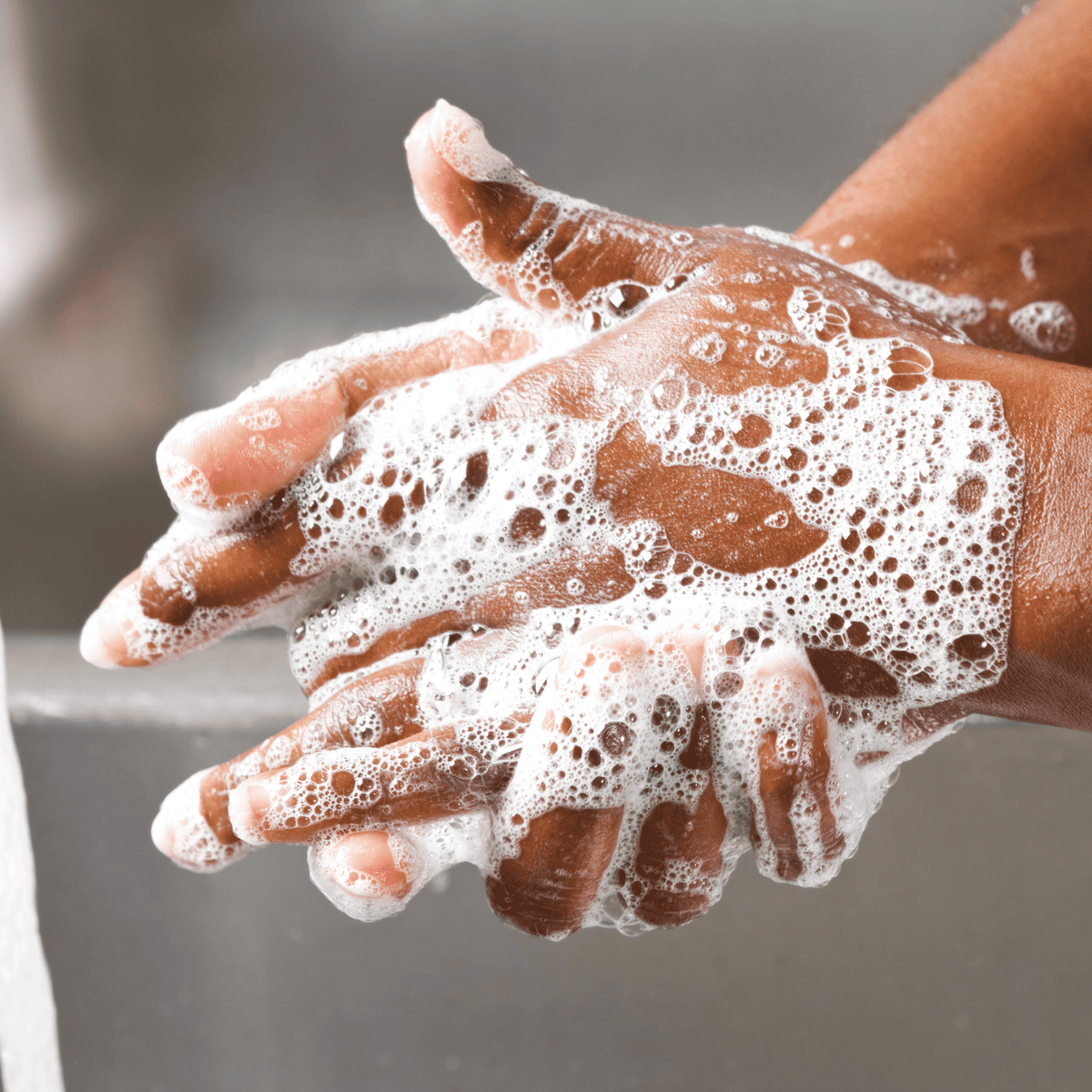 Mains à la peau foncée recouvertes de mousse de savon blanche, en train d'être lavées