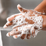Mains à la peau foncée recouvertes de mousse de savon blanche, en train d'être lavées